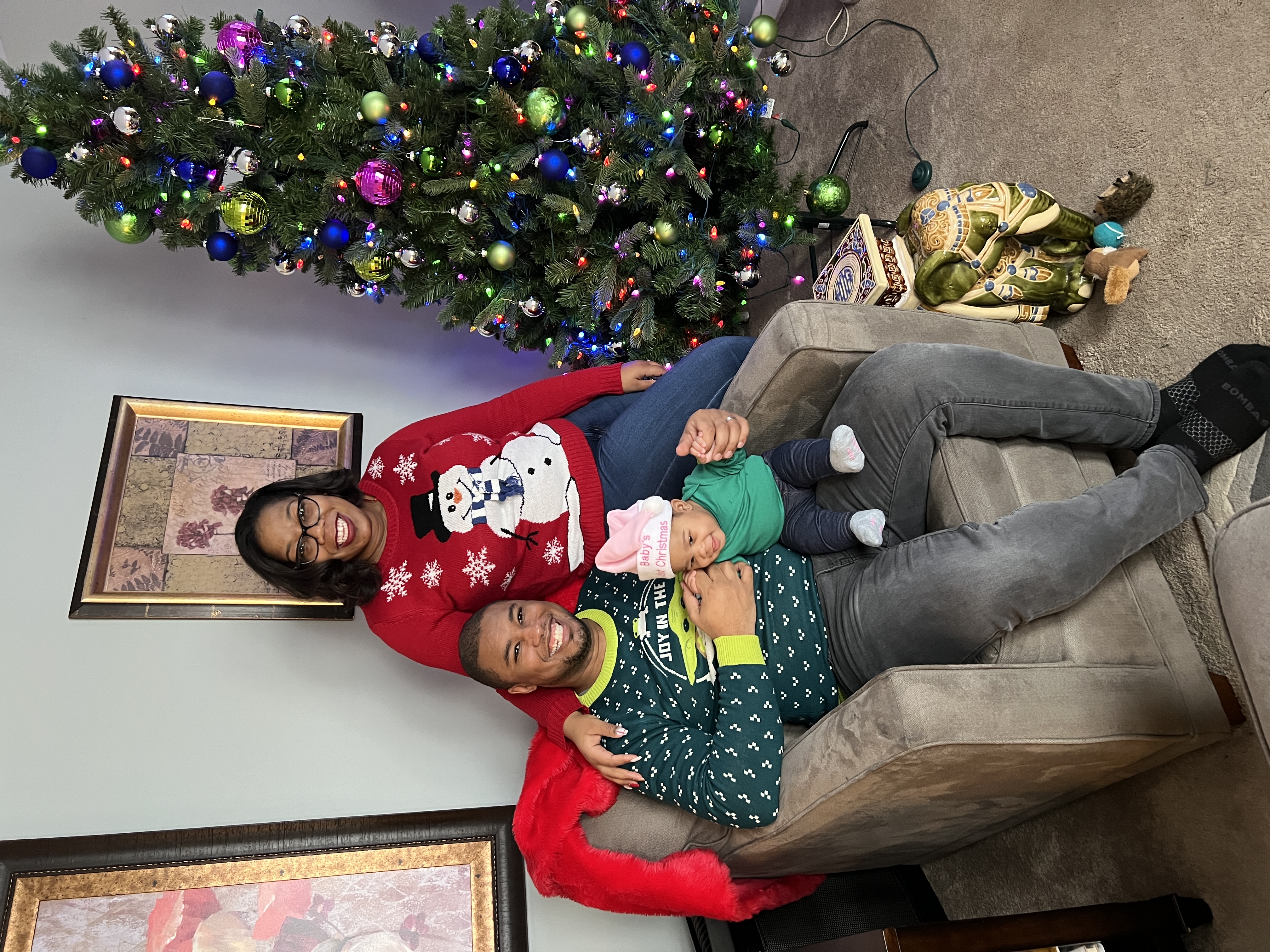 family christmas photo of someone sitting in a chair, another person sitting on the arm, holding a small child